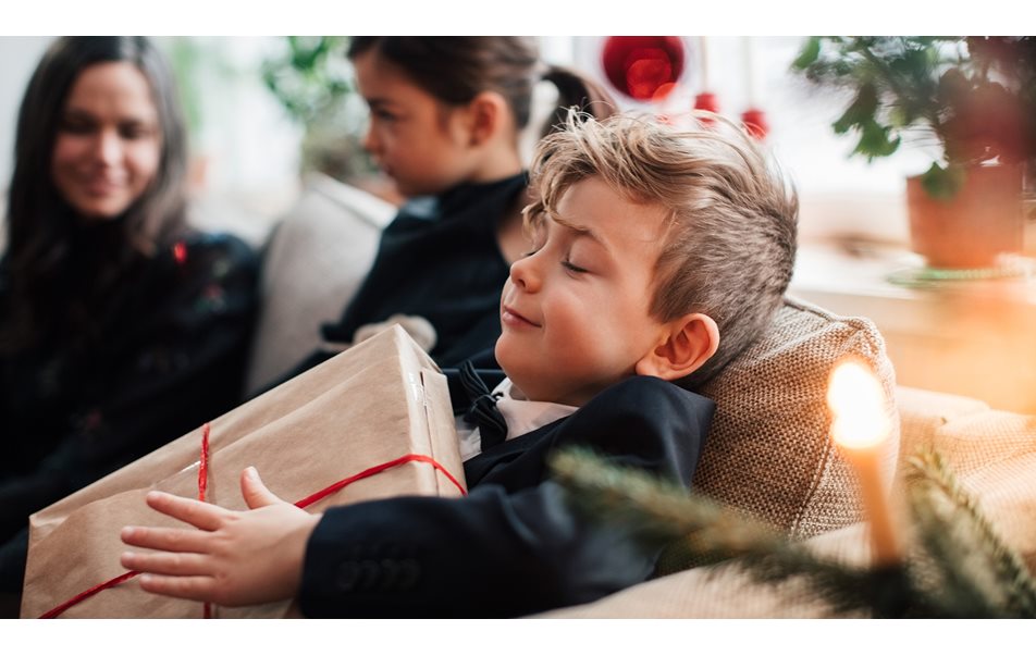 Gutt smiler mens han holder julegave mens han sitter med familien i stua.