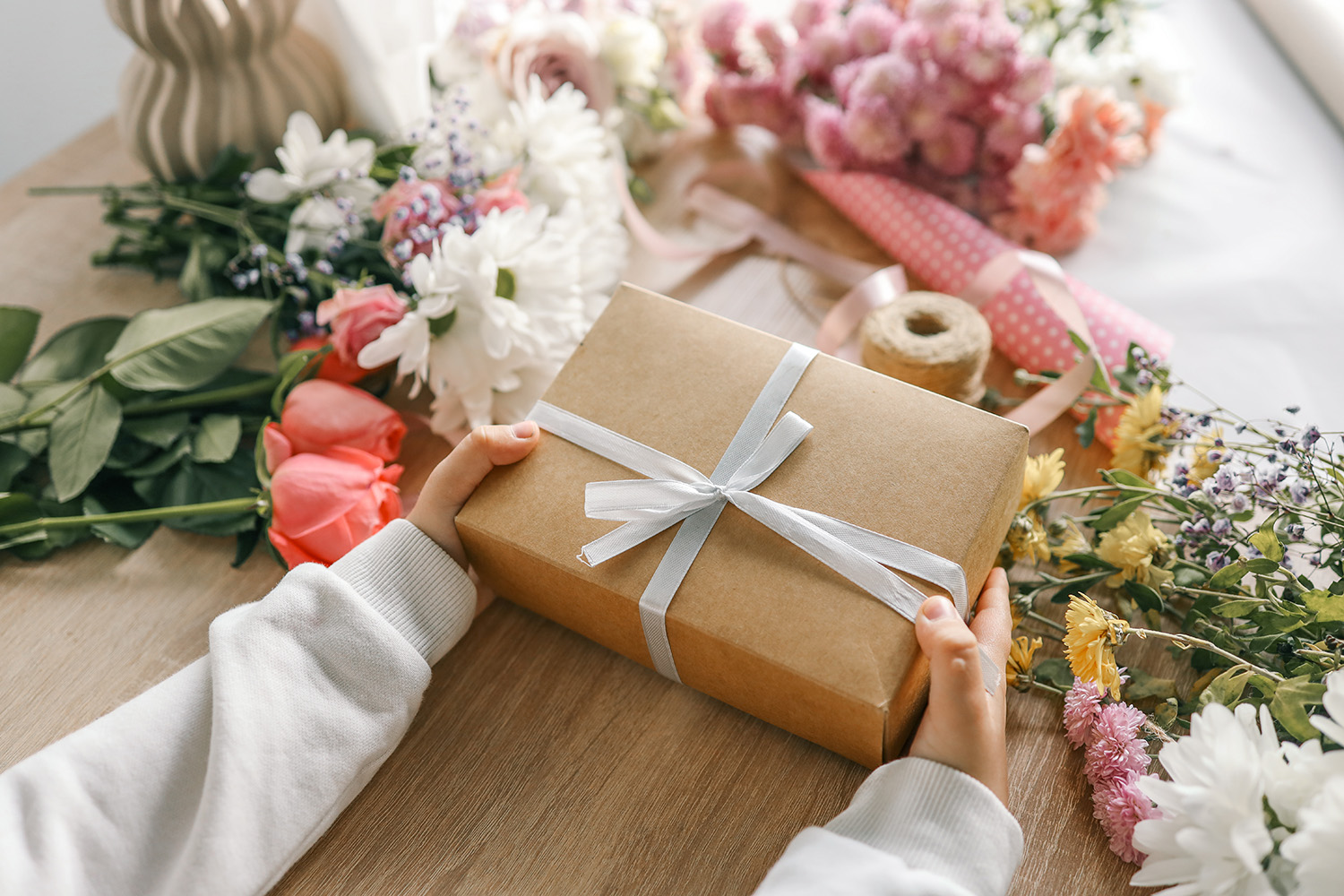 En person som holder en gaveeske med blomster og innpakningspapir spredt på bordet